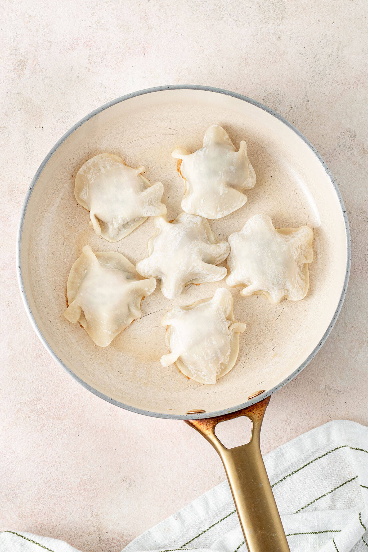 Gyoza wrappers laid over the balls of meat in the frying pan.