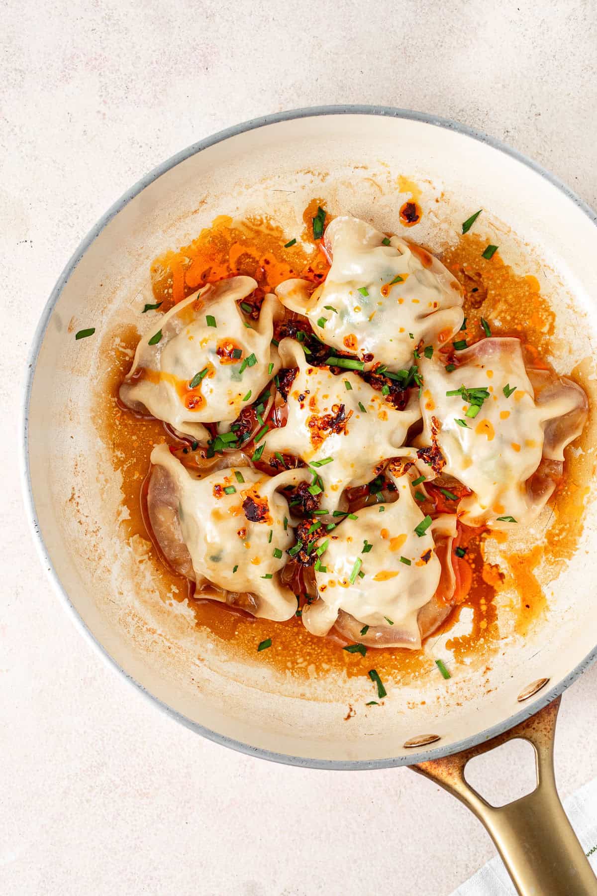 The cooked dumplings in the pan topped with chilli oil and chopped chives.
