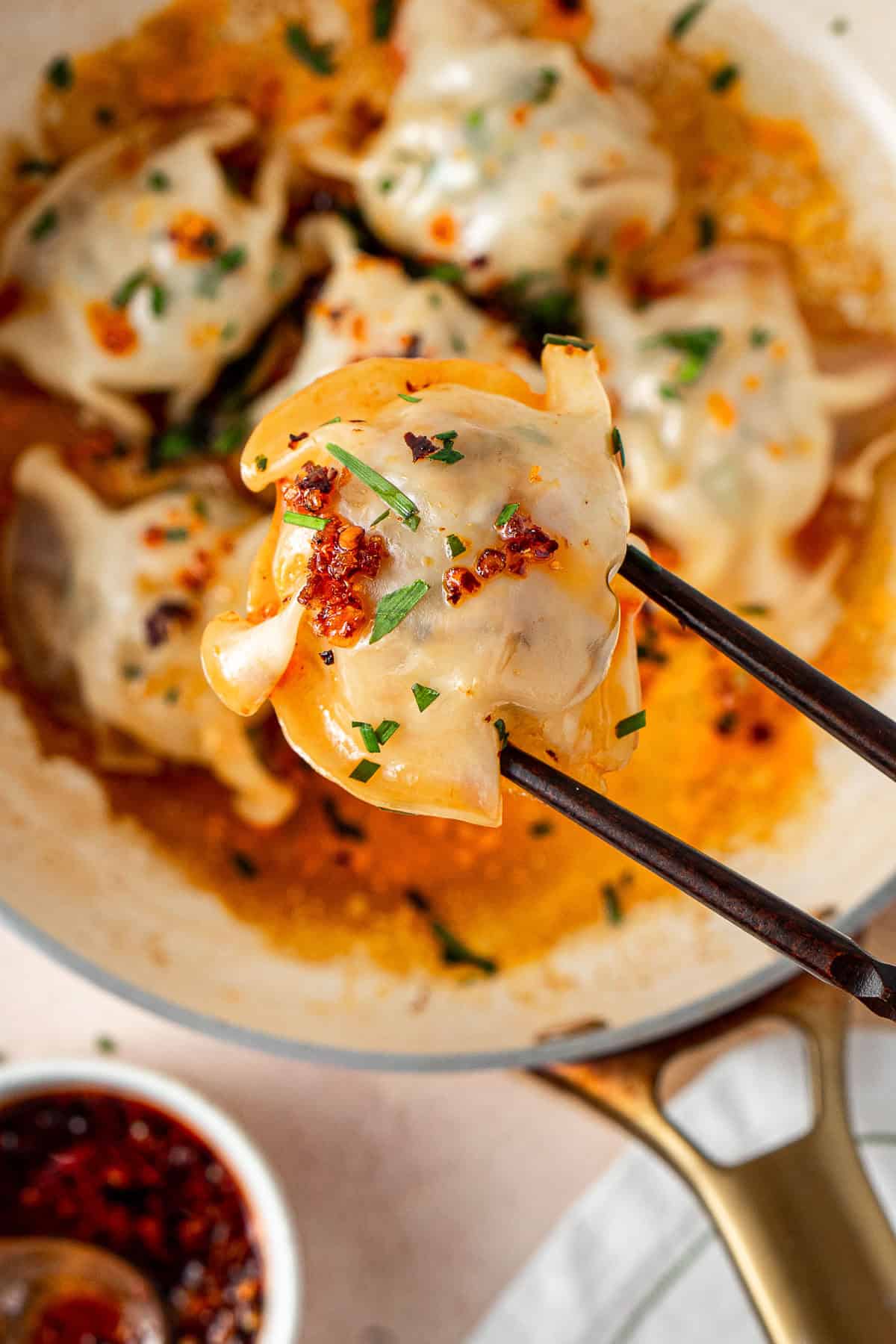 Chopsticks holding up a pork and chive blanket dumpling. 