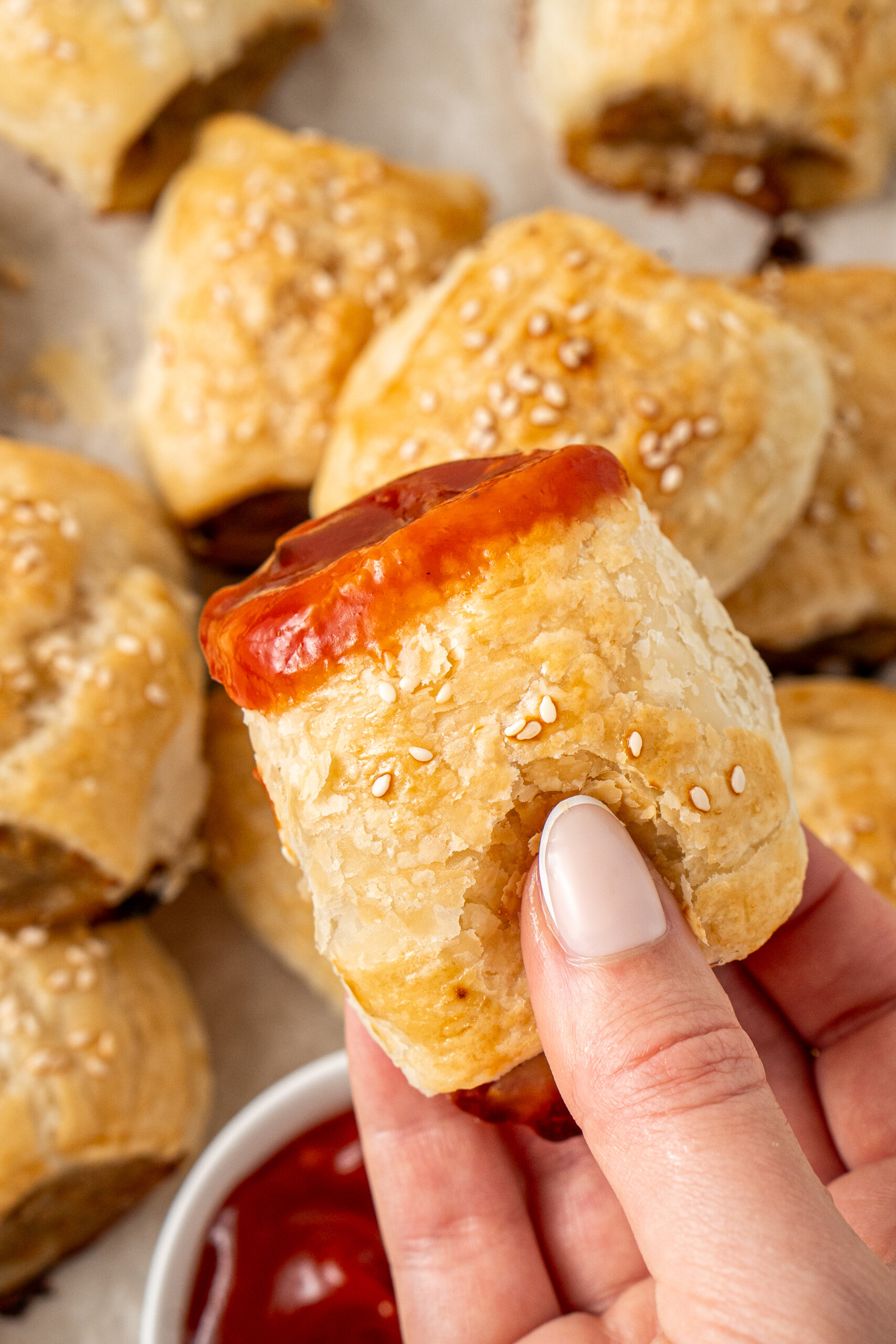 A hand holding a sausage roll dunked in tomato sauce.
