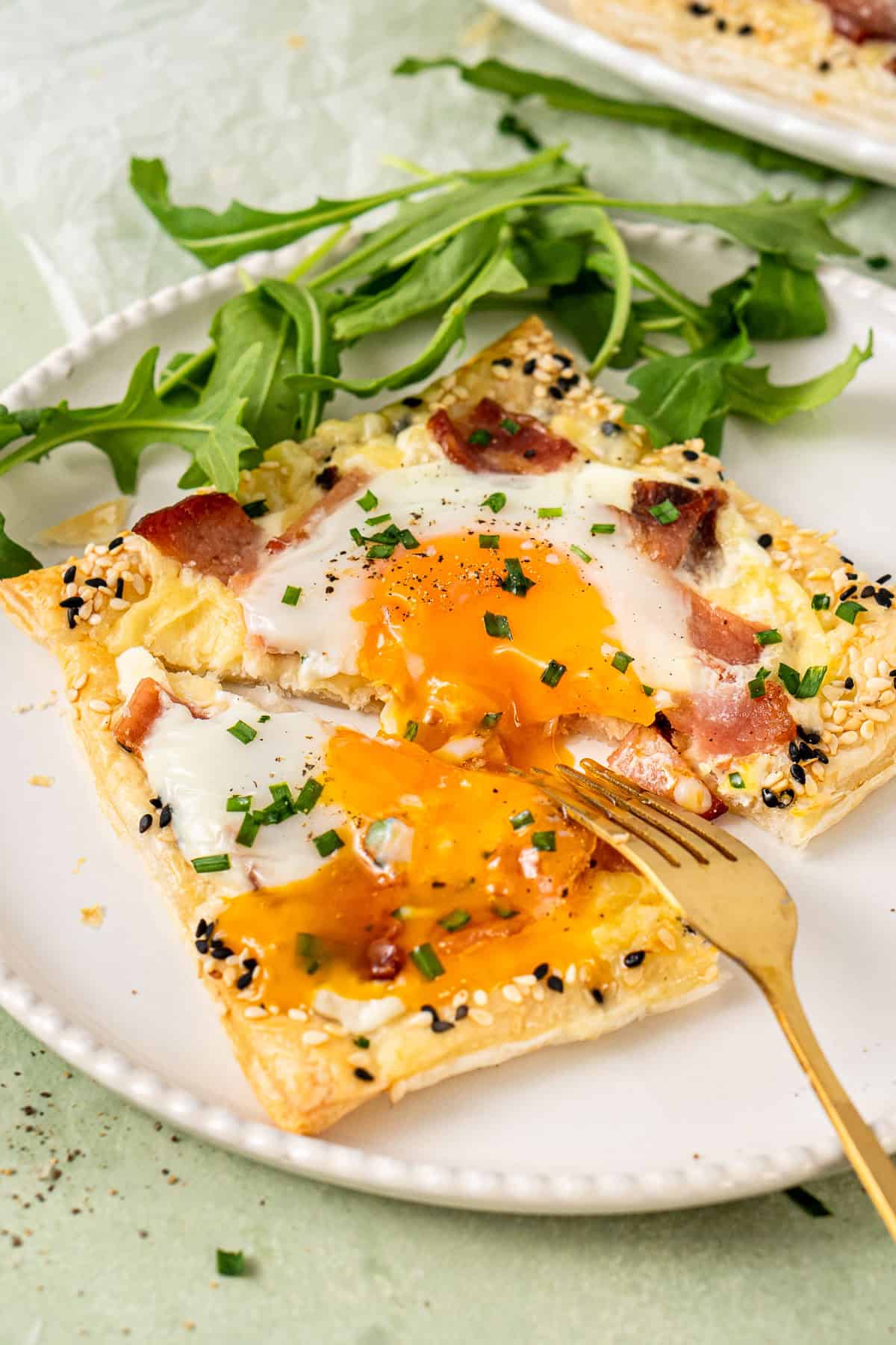 A fork breaking into the runny yolk in the breakfast tart on a white plate.
