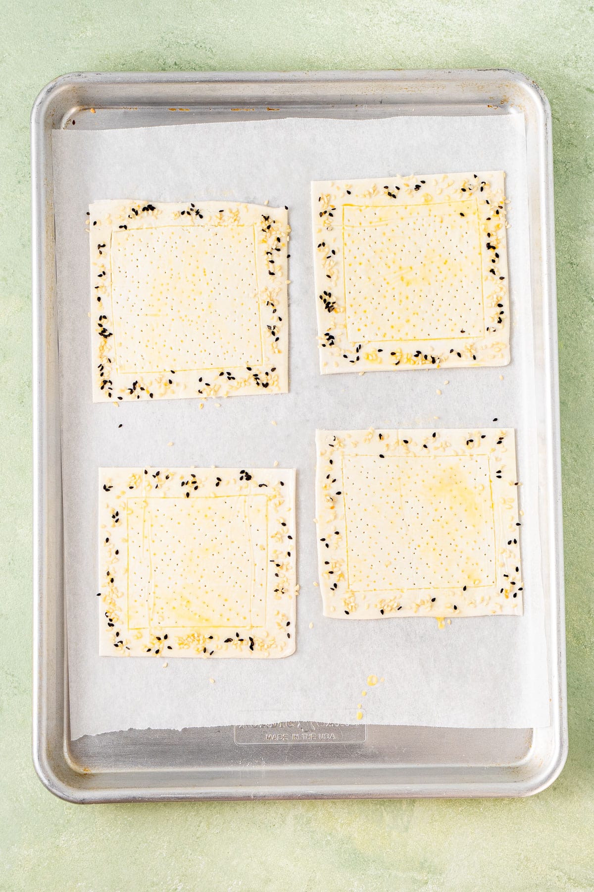 The pastry squares on a baking tray with sesame seeds.