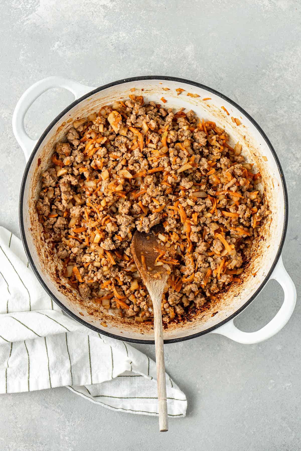 The pork mixture in the frying pan with a wooden spoon.