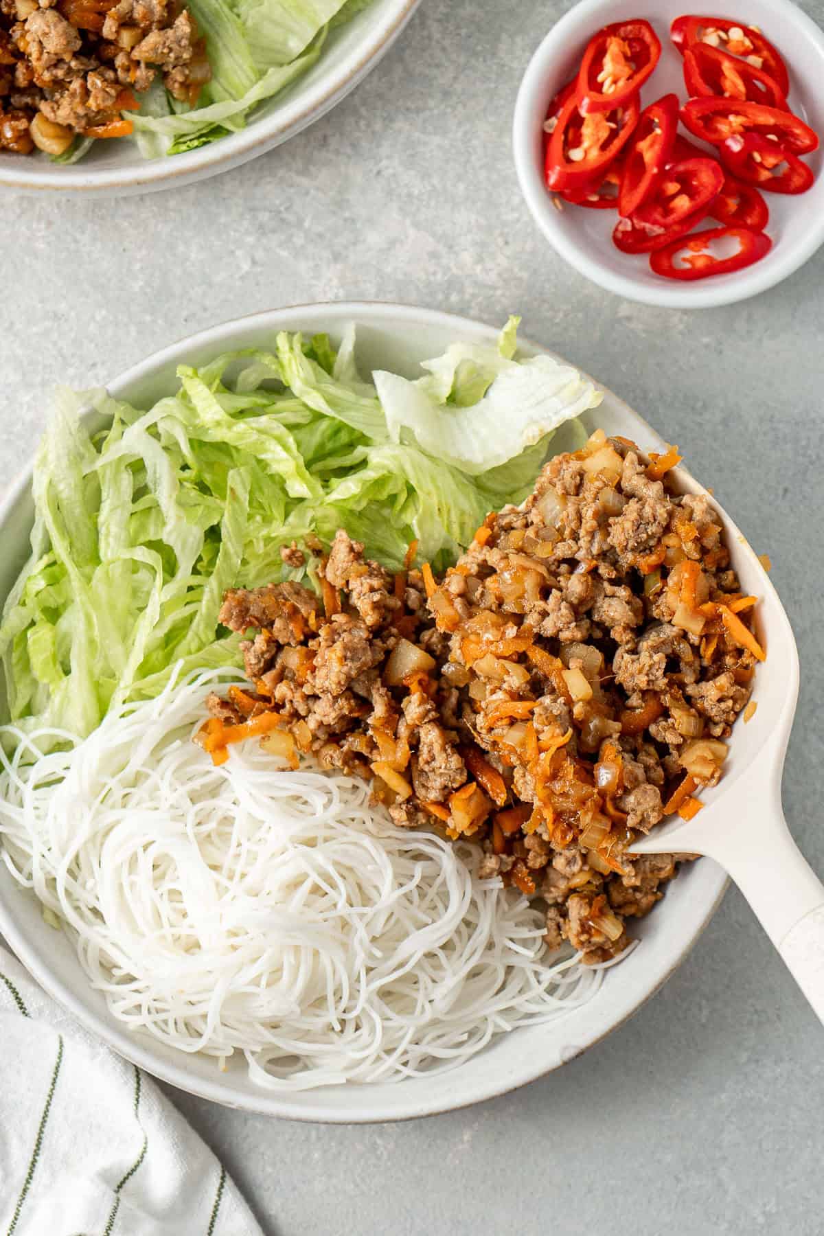 Spooning the pork mixture over the noodles and lettuce.