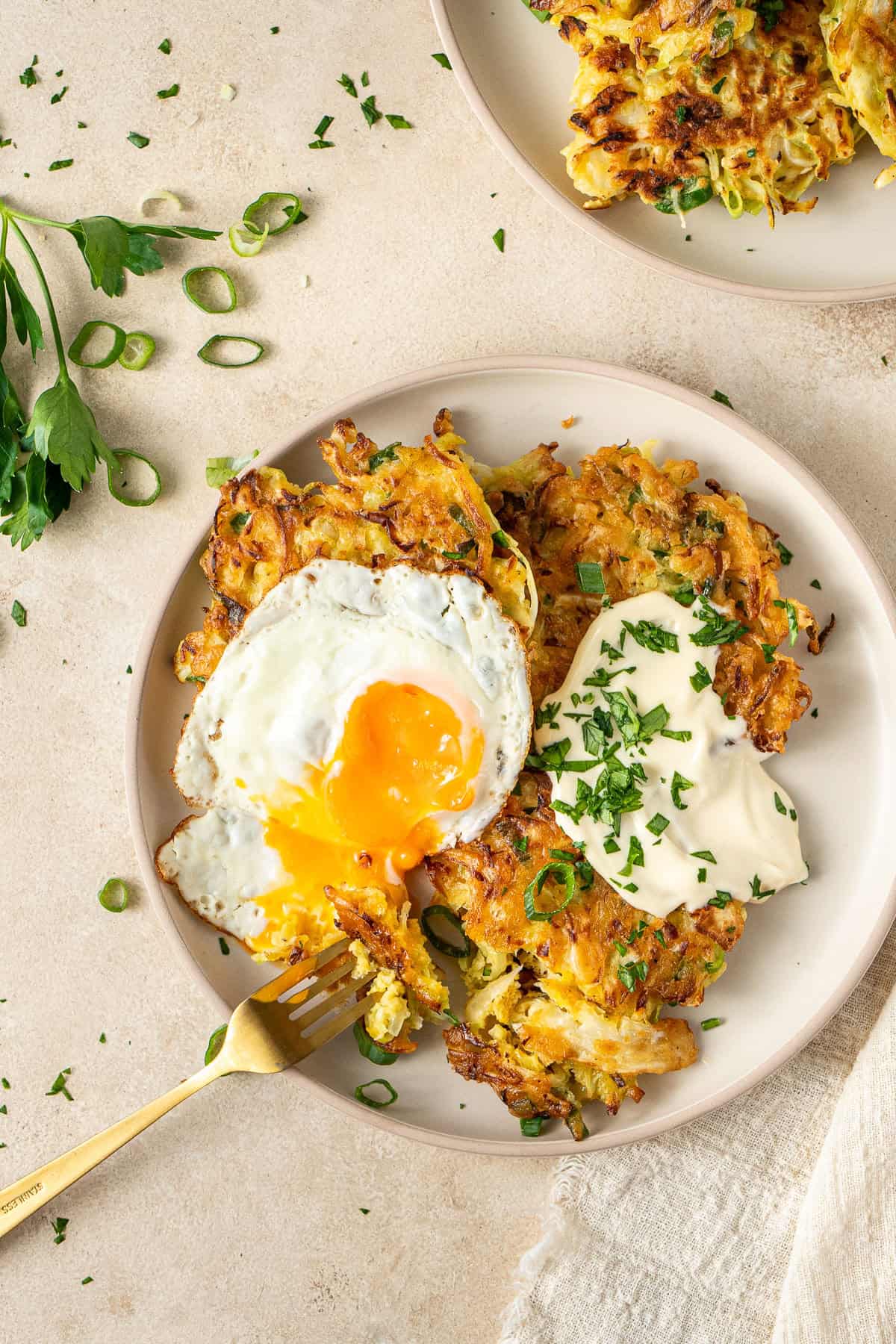 The cabbage fritters on a plate with mayo and a fried egg broken with a fork.