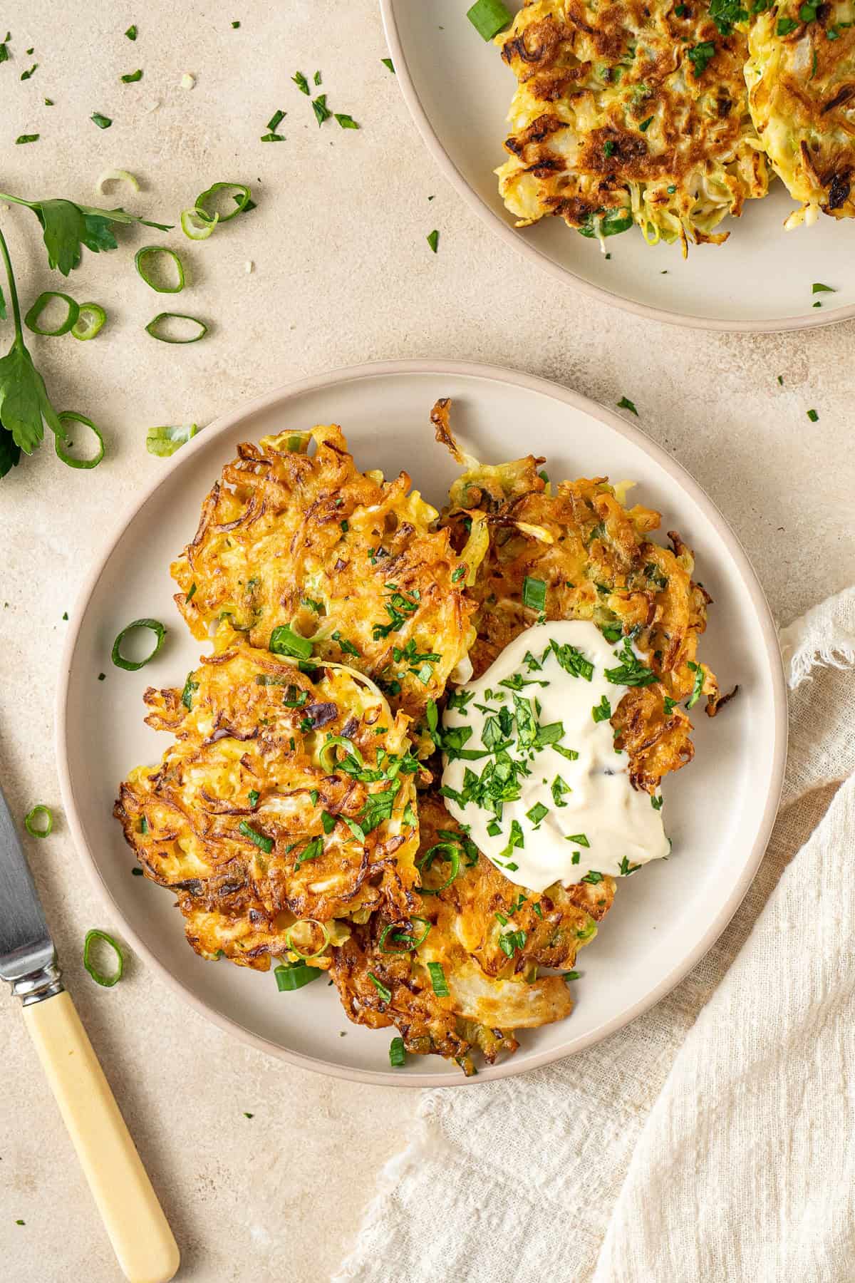 Four cabbage fritters on a plate with mayo and fresh herbs.