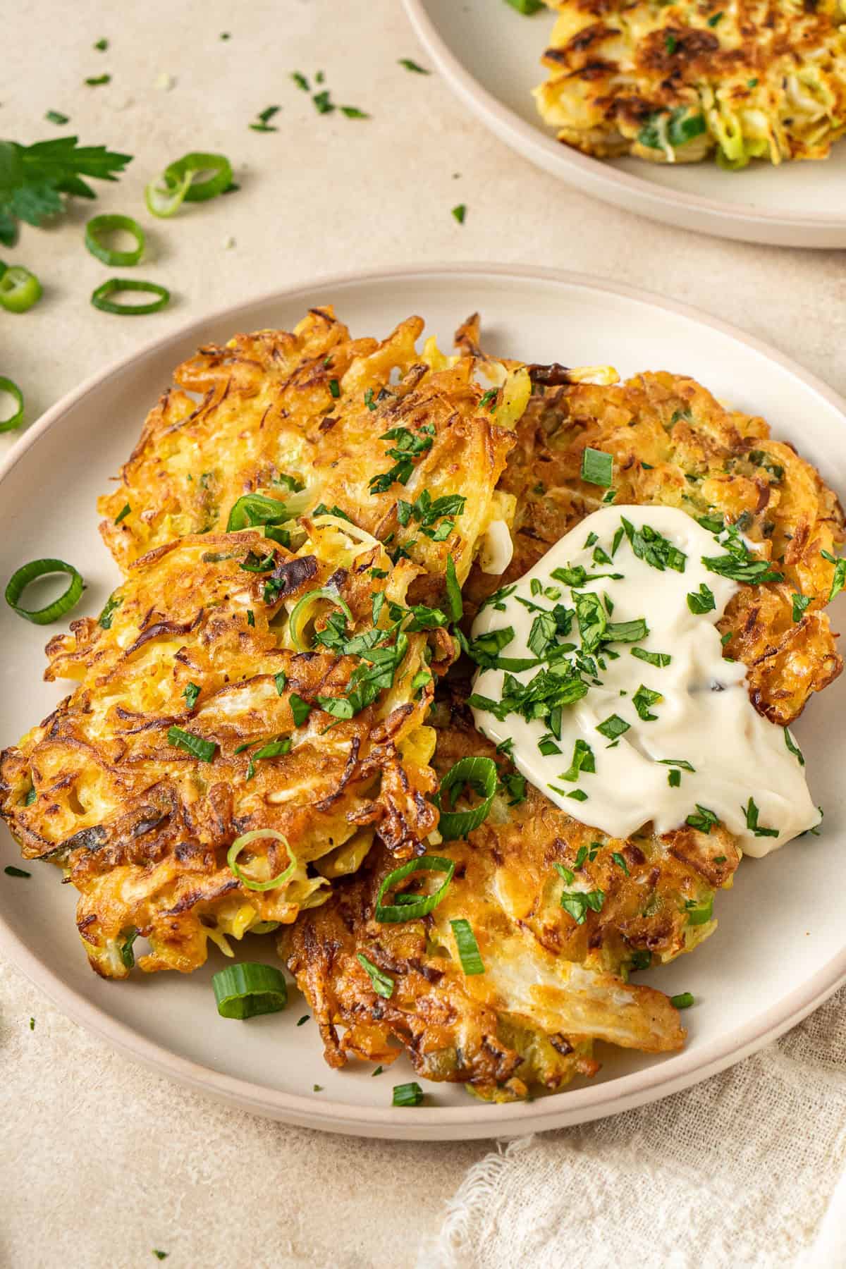 Four cabbage fritters on a plate with mayonnaise and fresh herbs.