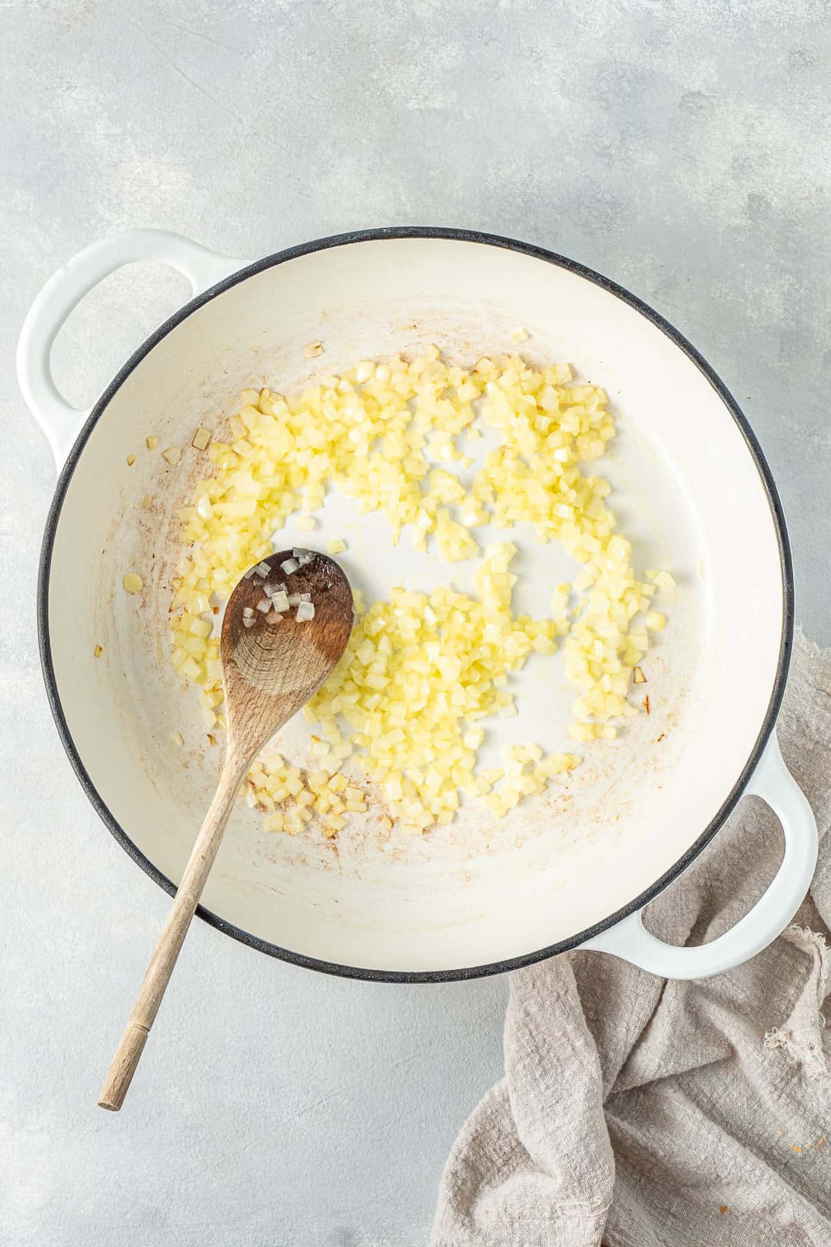 The onions frying in a pan with a wooden spoon.