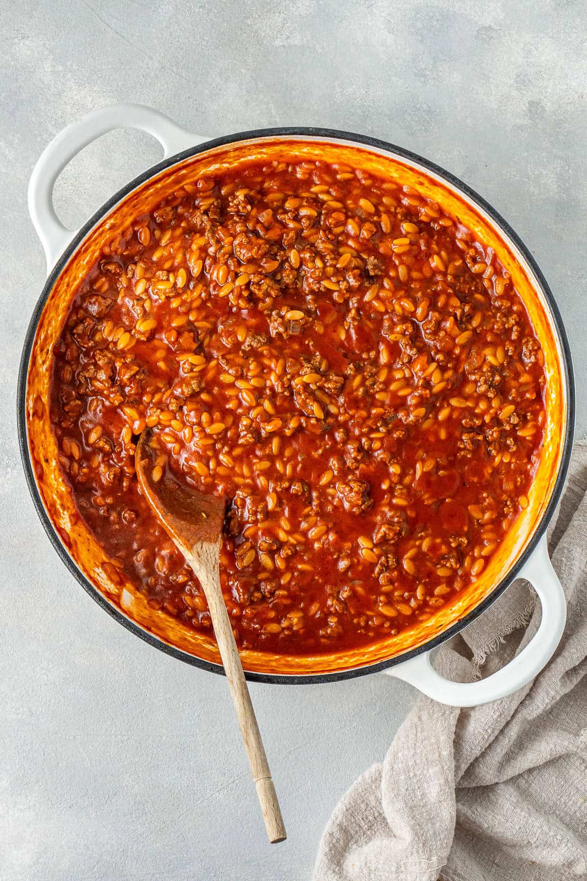 The cooked orzo in the sauce with a wooden spoon.