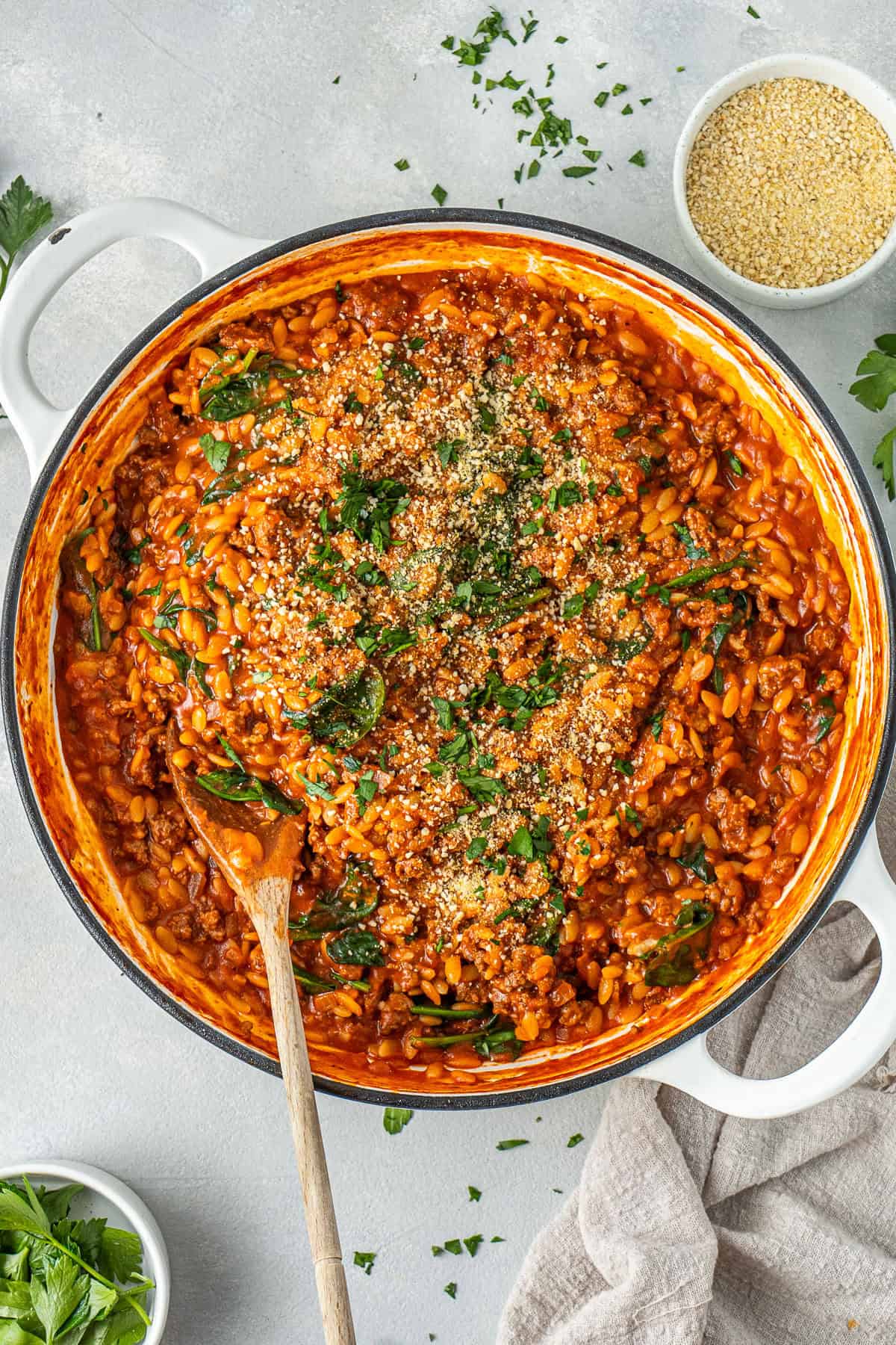 The cooked ground beef and orzo in a pot with a wooden spoon topped with dairy free parmesan and parsley.