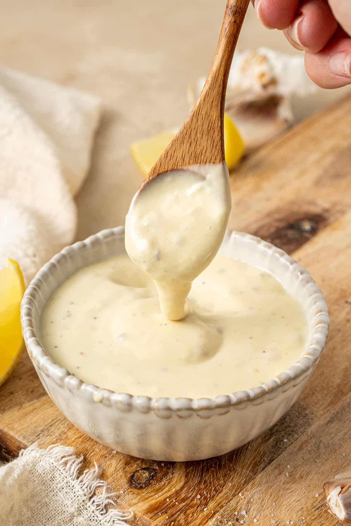 A spoon drizzling the dairy free caesar salad dressing from a bowl.