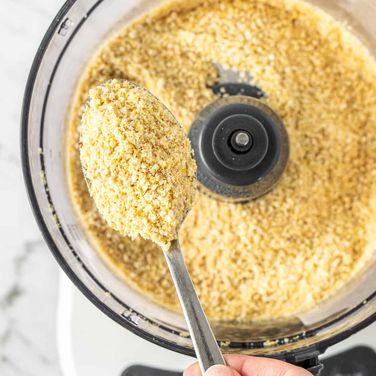 A spoon scooping up the dairy free parmesan cheese from the food processor.