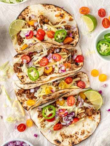 Ground beef tacos with cheese, tomato and onions.