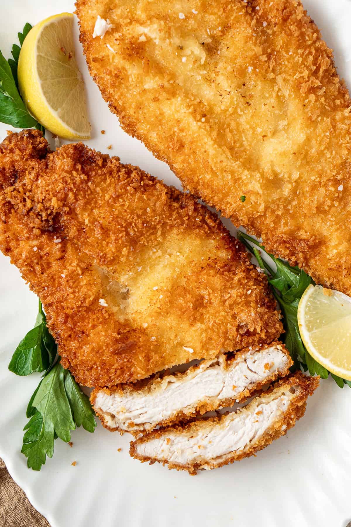 Chicken schnitzel cut into sliced on a white plate.
