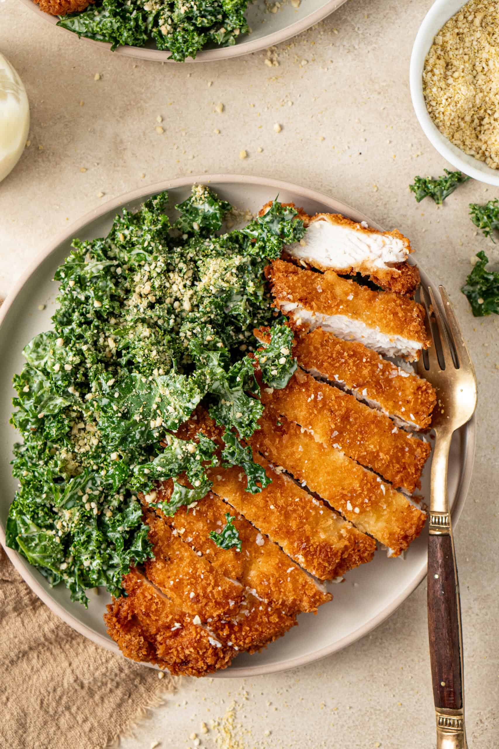 Sliced chicken schnitzel on a plate with kale caesar salad.