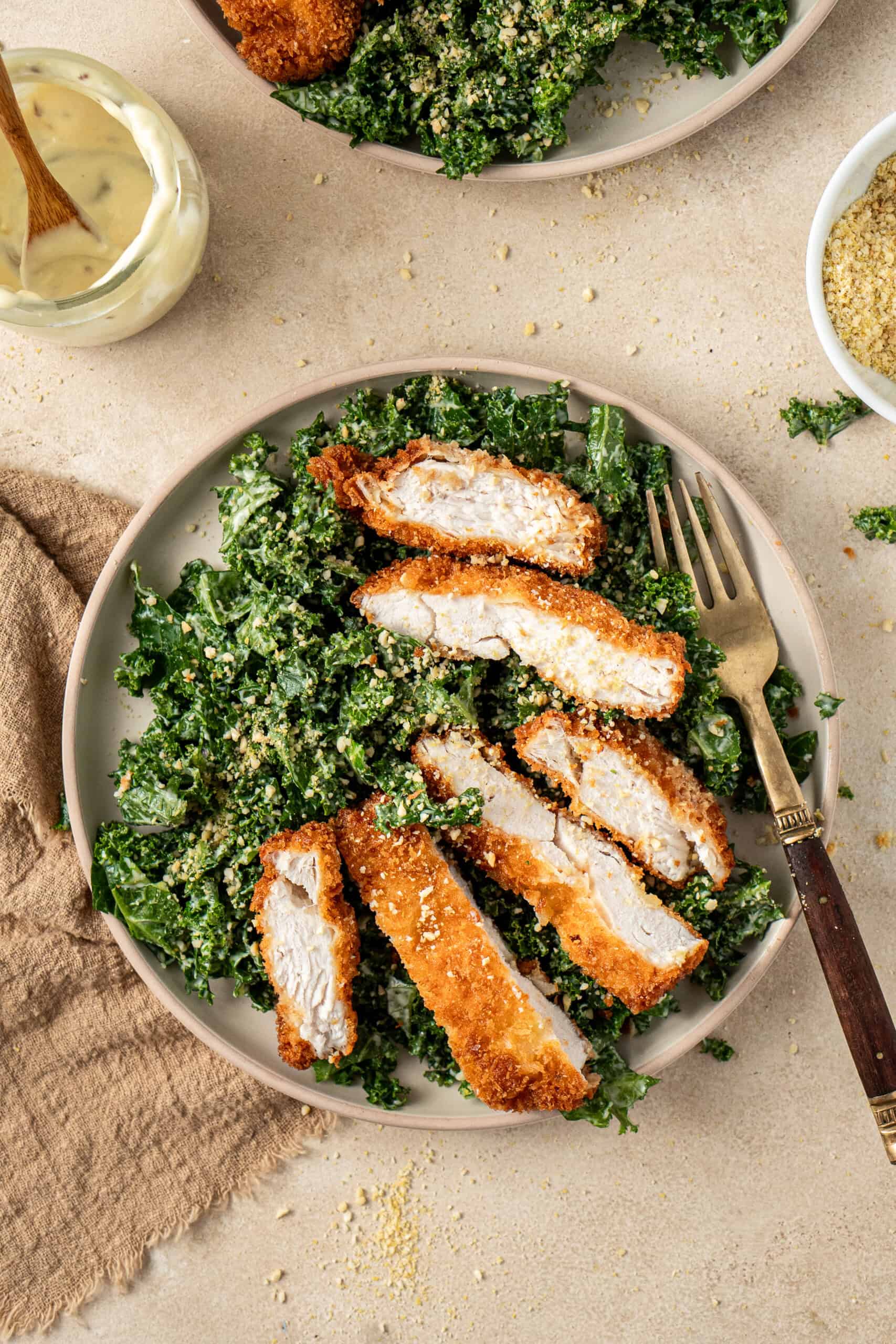 Sliced chicken schnitzel with kale caesar salad on a plate.