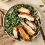 Sliced chicken schnitzel with kale caesar salad on a plate.