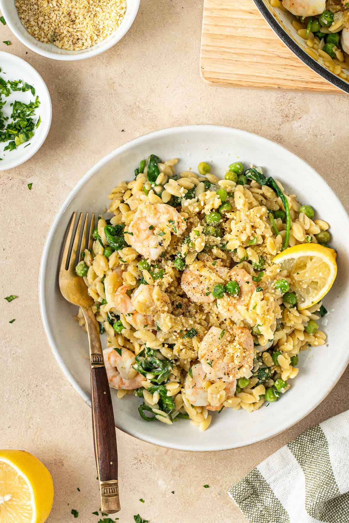 Lemon prawn orzo in a bowl with a fork and a wedge of lemon.
