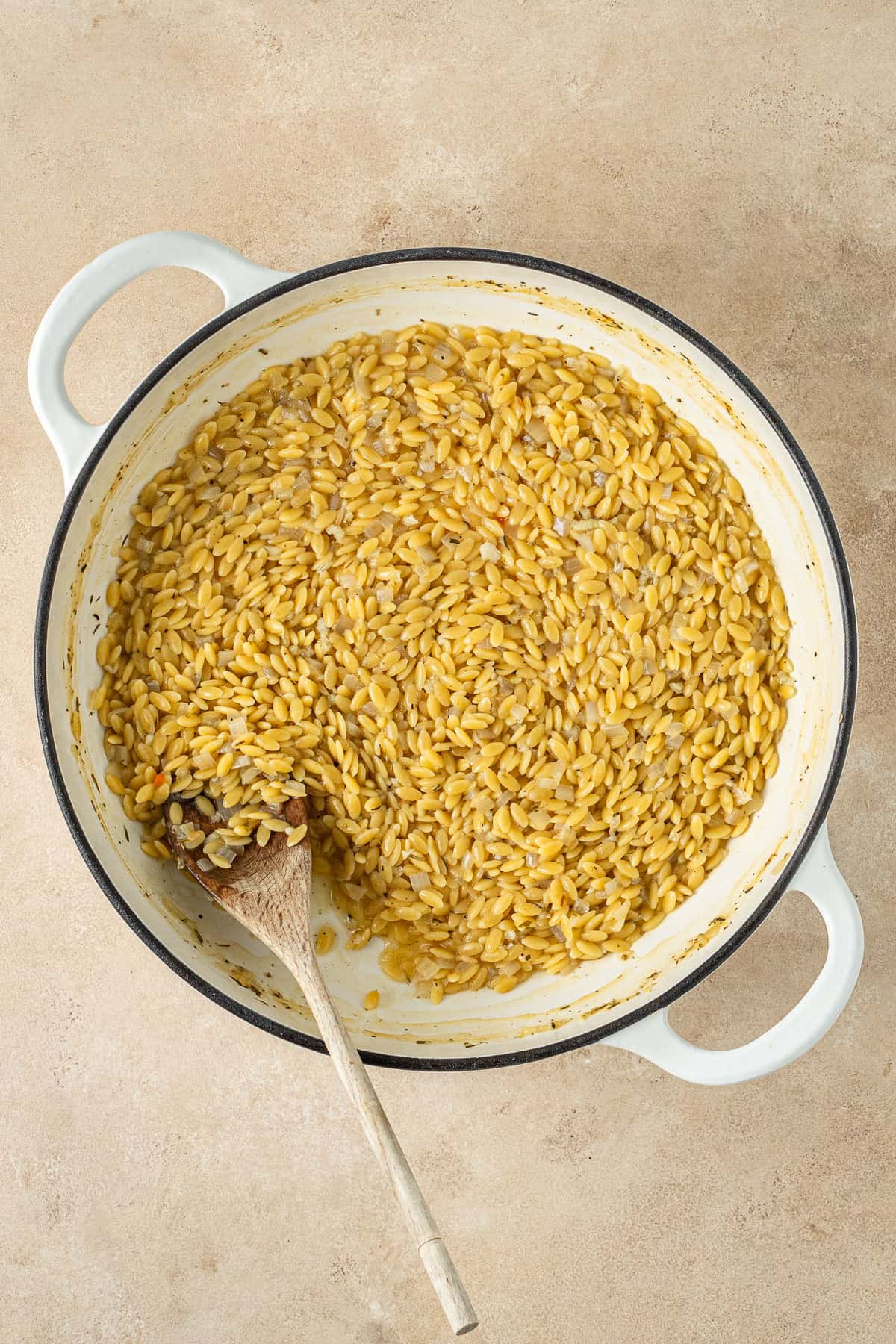 The cooked orzo in the pan with a wooden spoon.