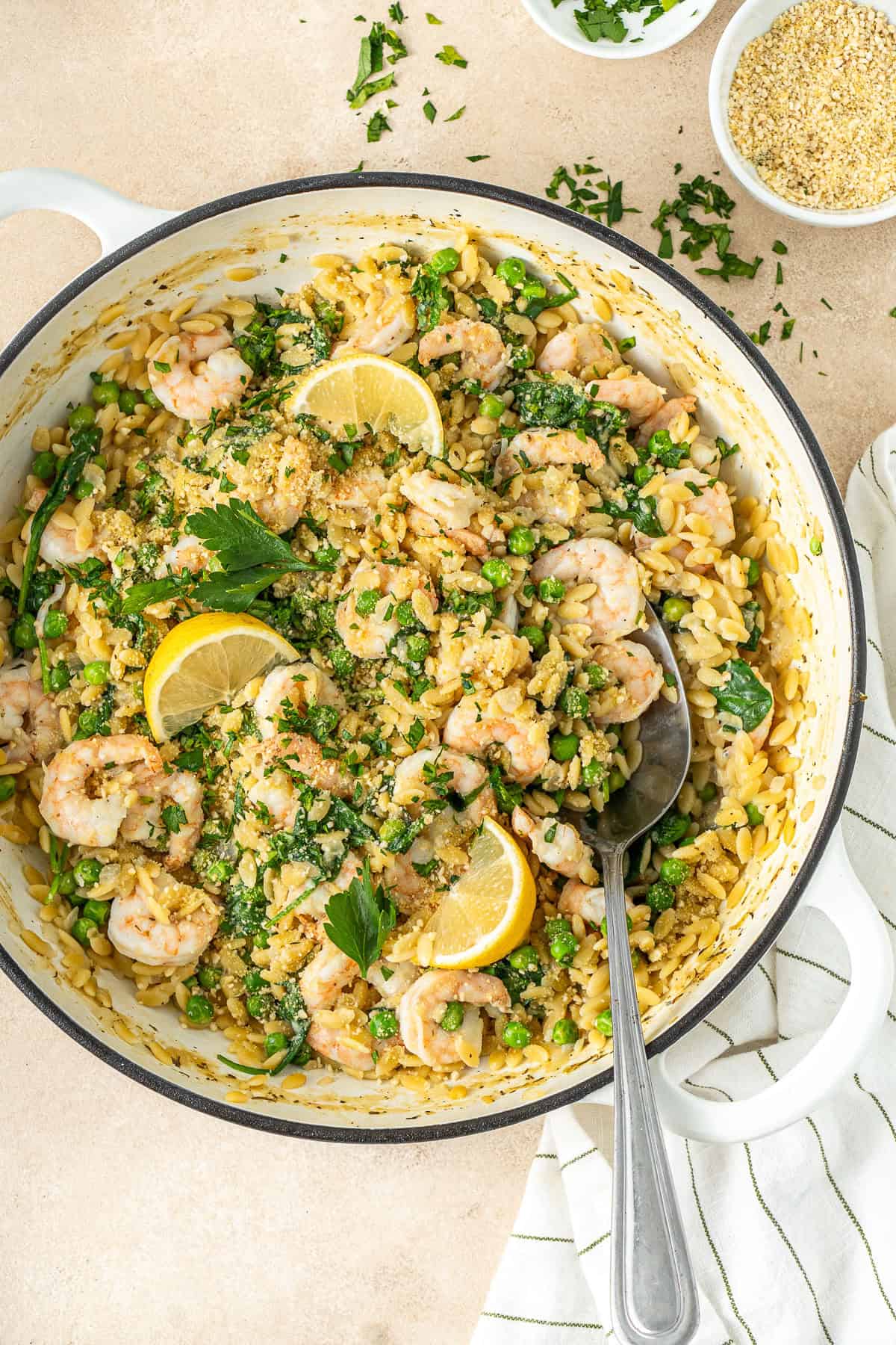 Lemon prawn orzo in a pan with lemon wedges and a serving spoon.