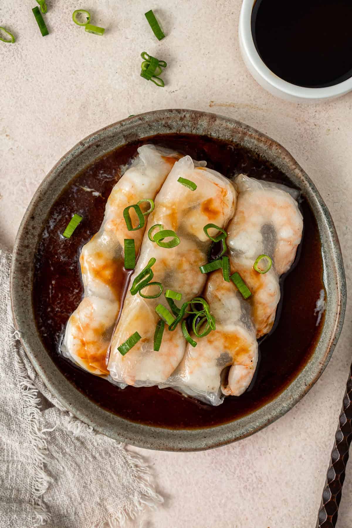 Three steamed prawn rolls with dipping sauce and spring onions on a plate.