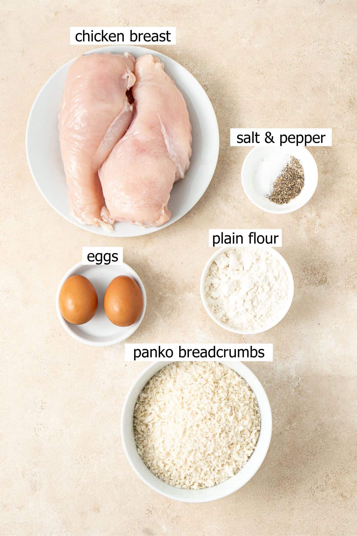 All ingredients needed to make chicken schnitzel laid out in bowls.