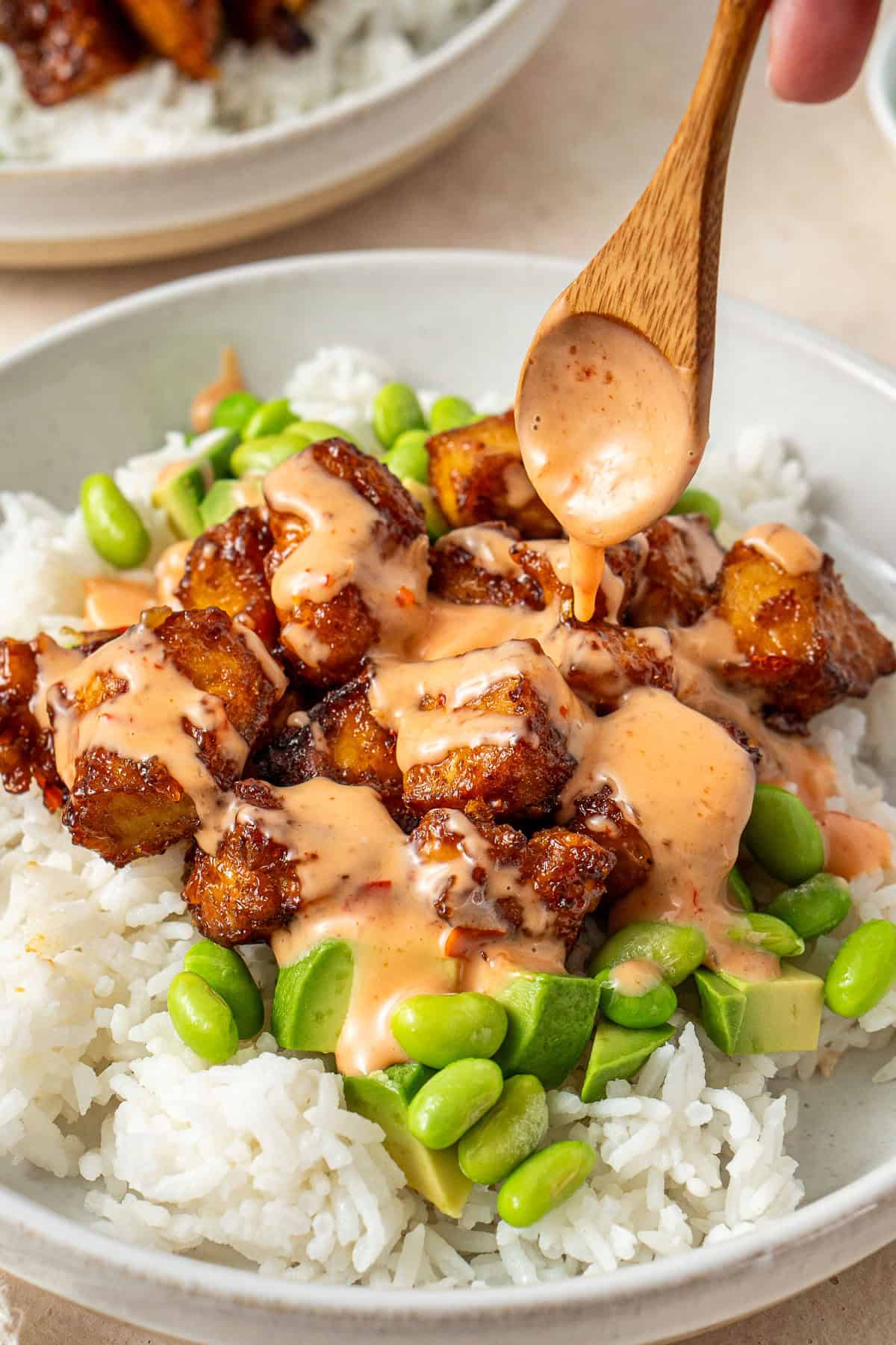 Spooning the extra bang bang sauce over the tofu rice bowls.