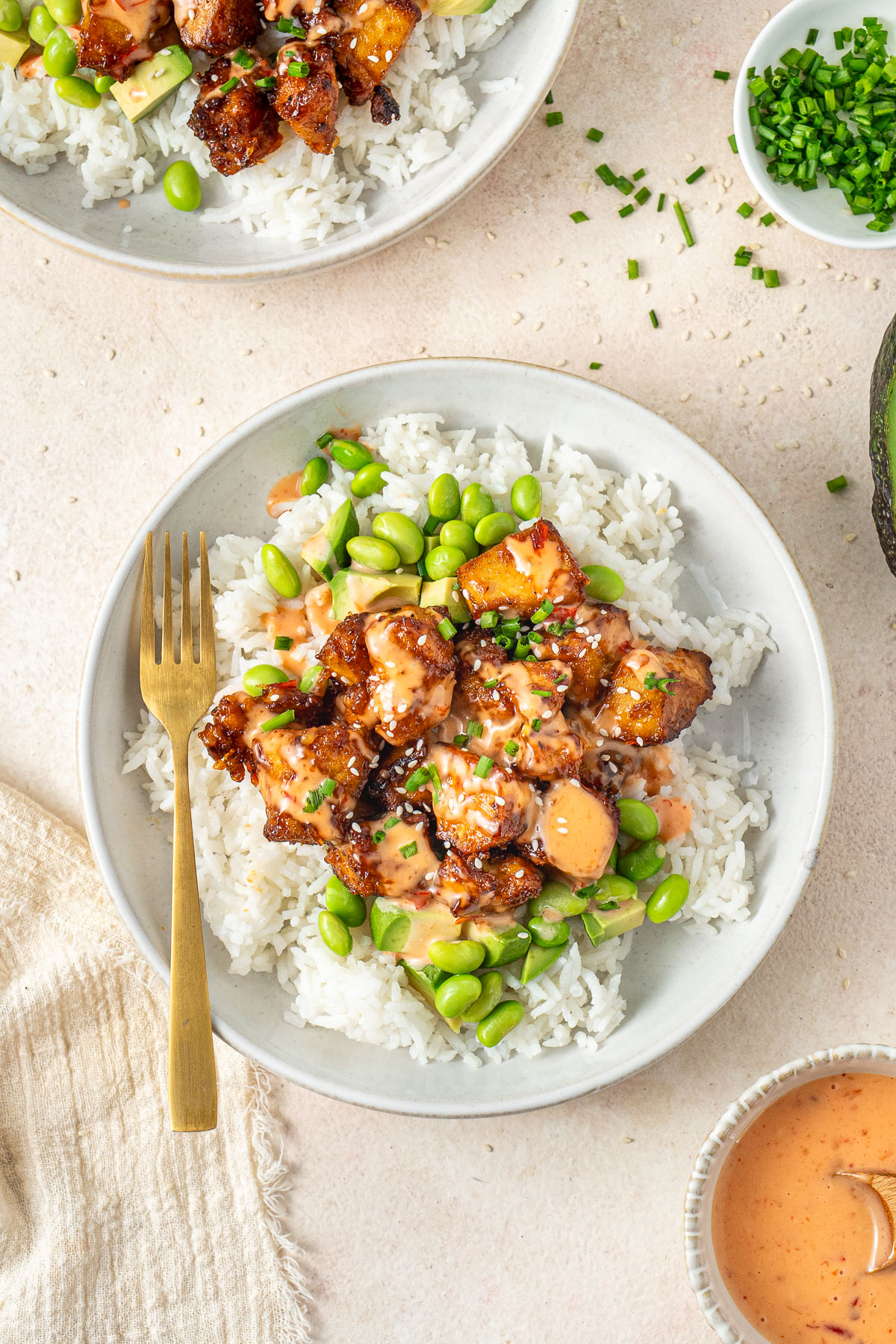 Bang bang tofu served in a bowl with edamame, avocado and rice with a gold fork.