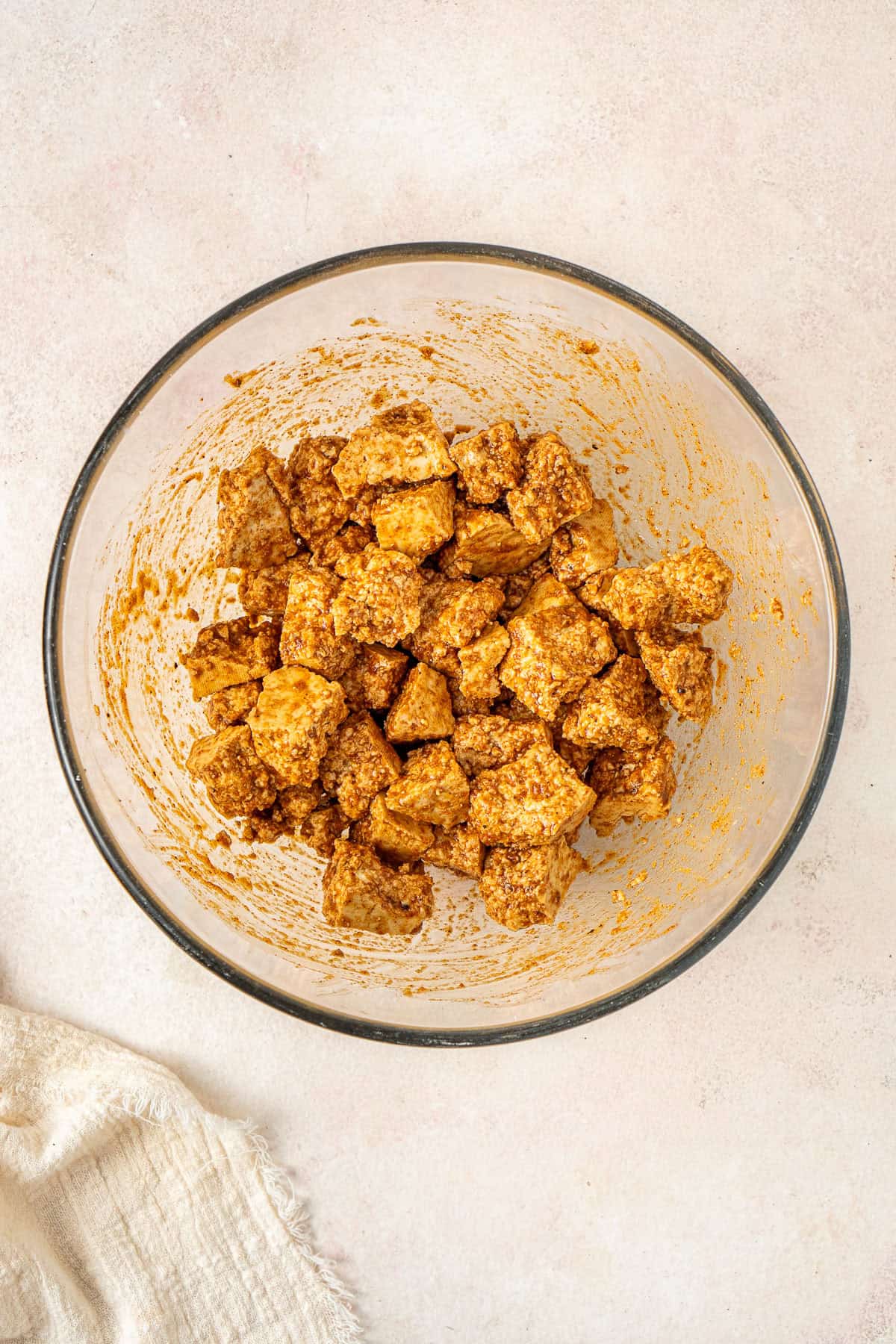 The tofu pieces in a large glass bowl mixed with spices.