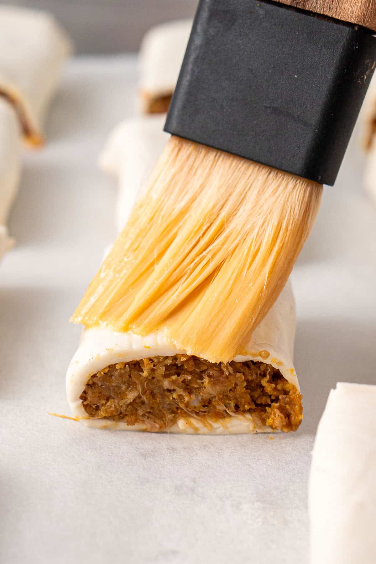 Brushing the beef sausage roll with egg wash.