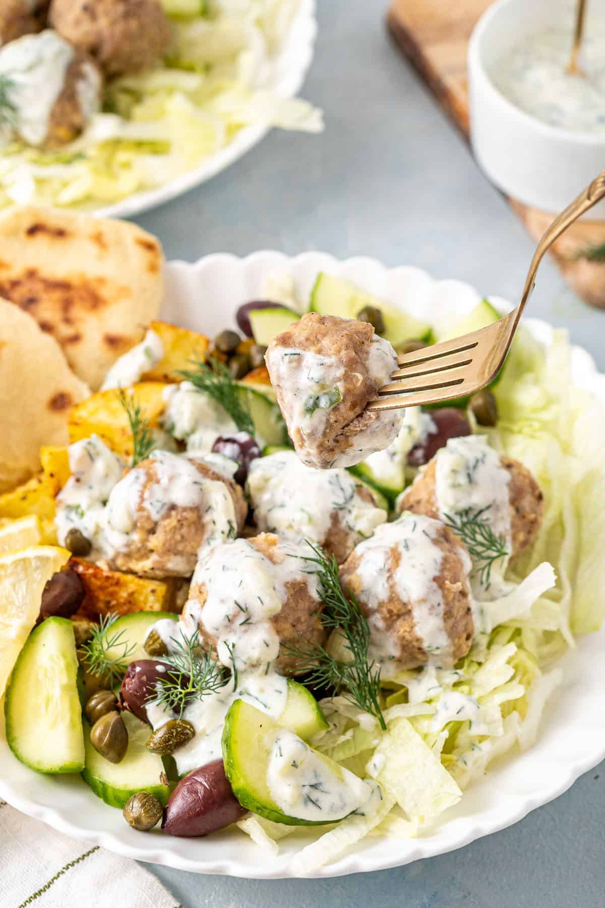 A fork picking up a meatball out of a bowl.