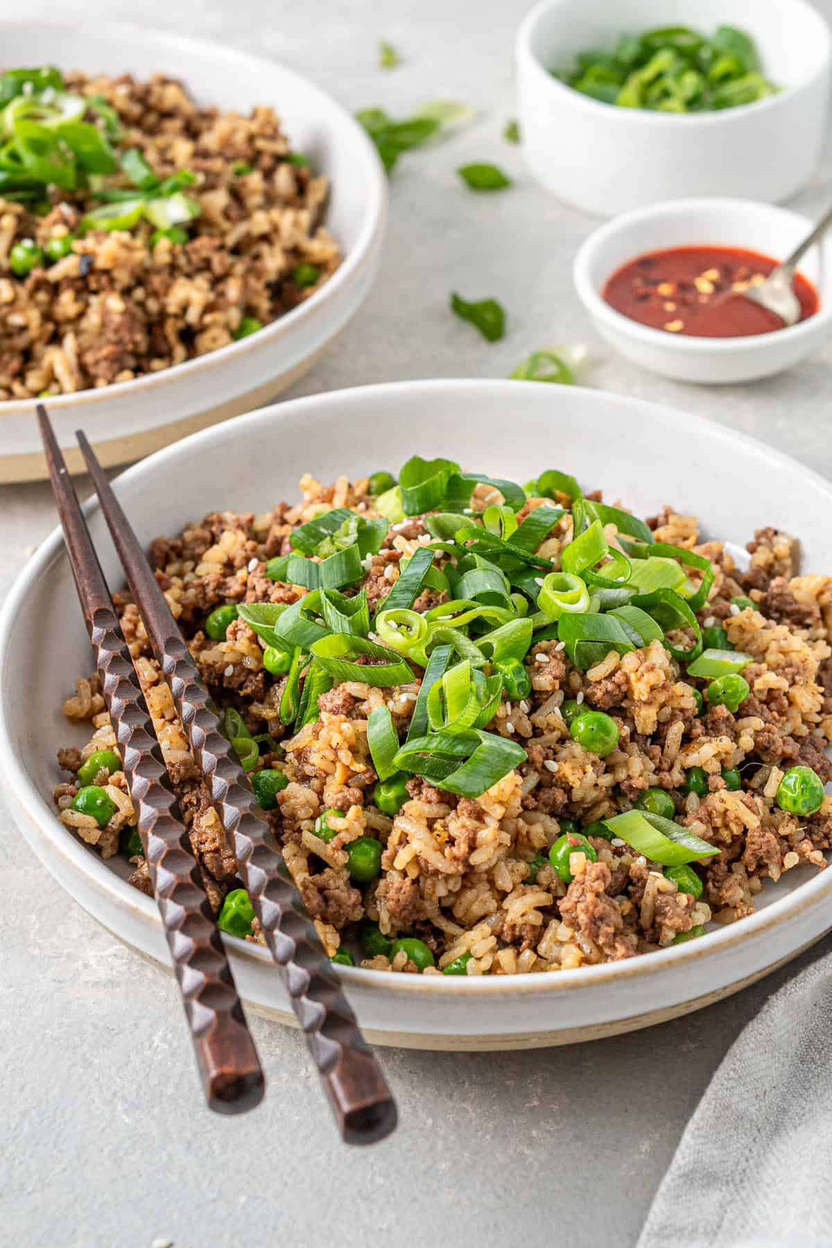 Ground beef fried rice served into bowls with spring onions and chopsticks.