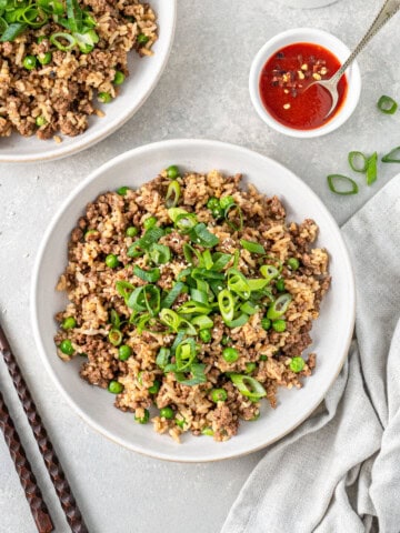 Ground beef fried rice served into bowls withy spring onions on top and sriracha on the side.