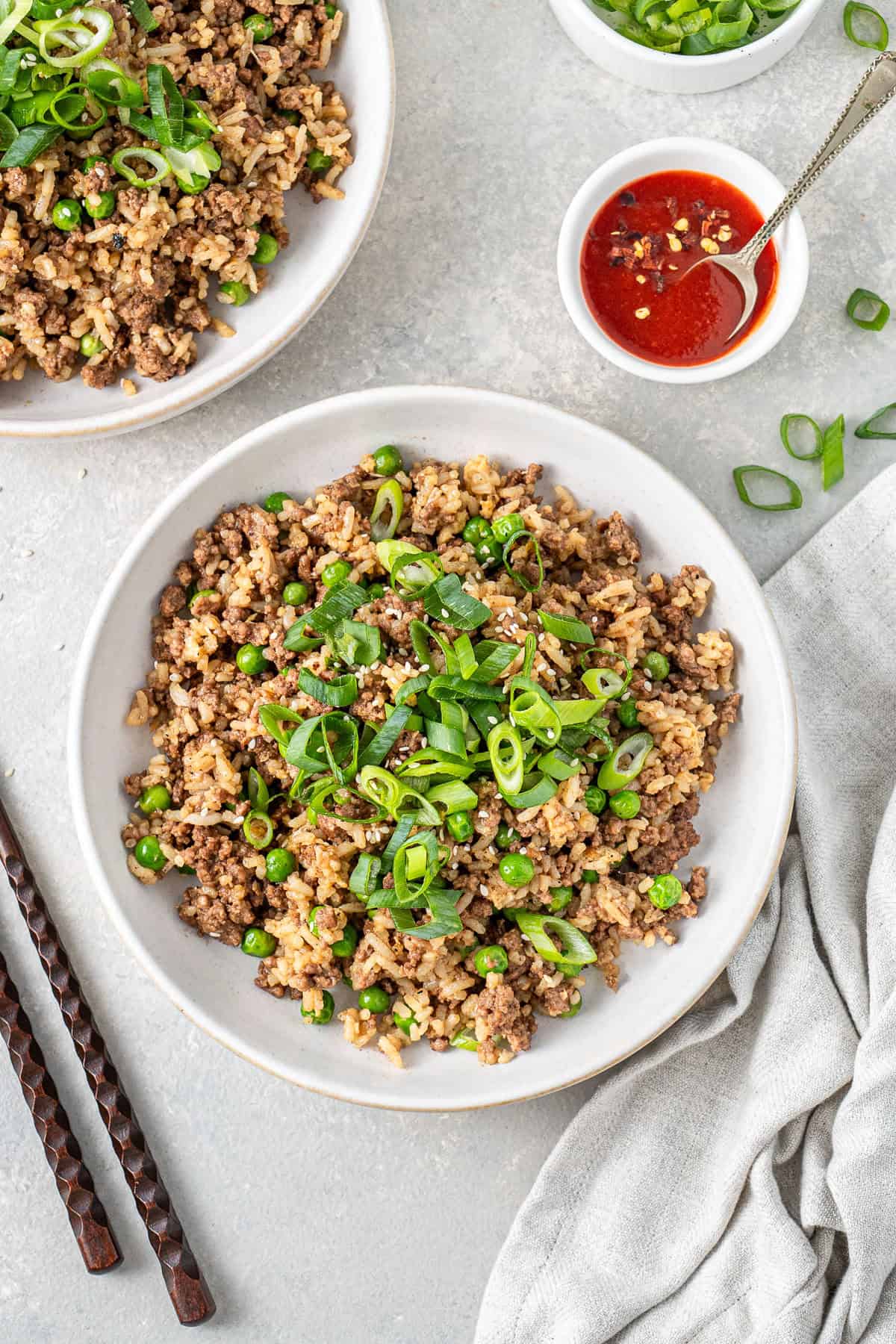 Ground beef fried rice served into bowls withy spring onions on top and sriracha on the side. 