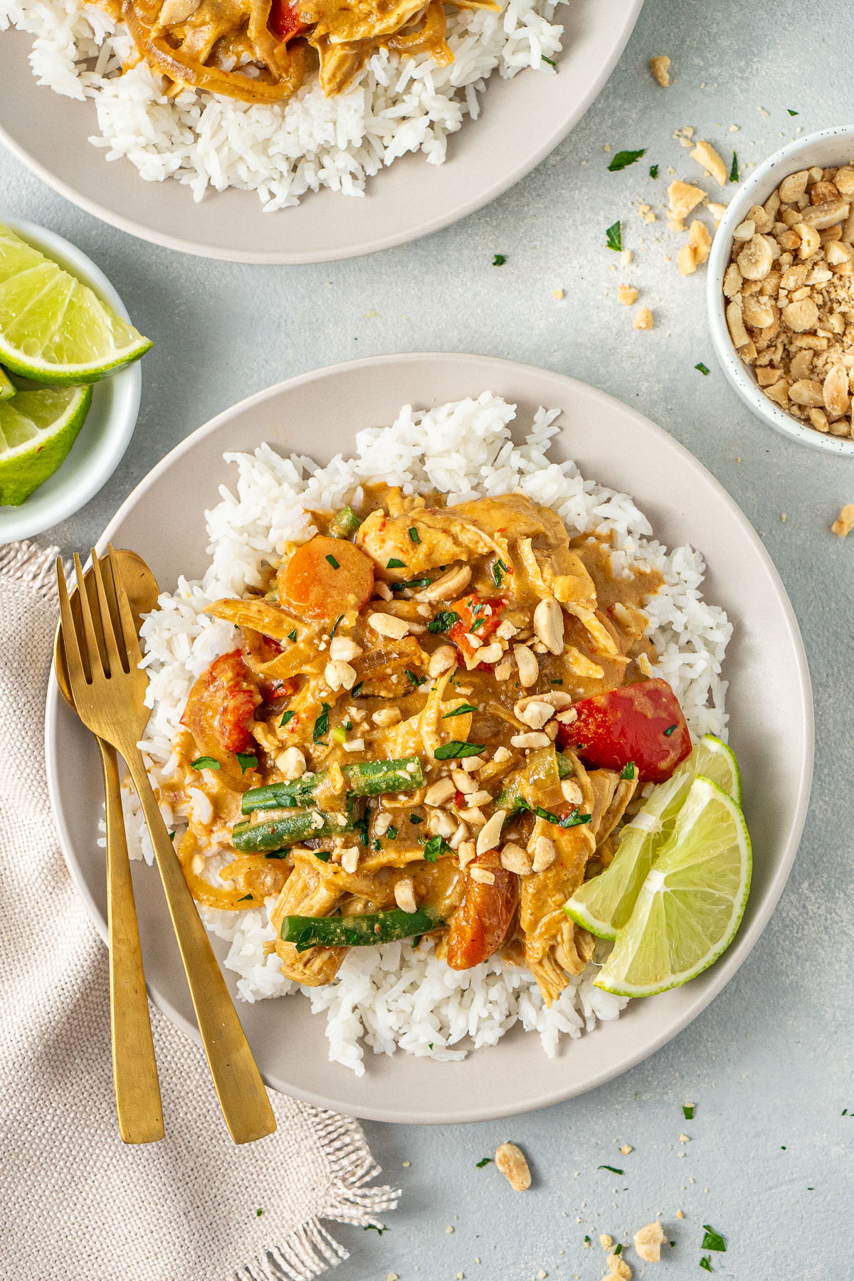 Slow cooker satay chicken served over rice with lime wedges and gold cutlery.