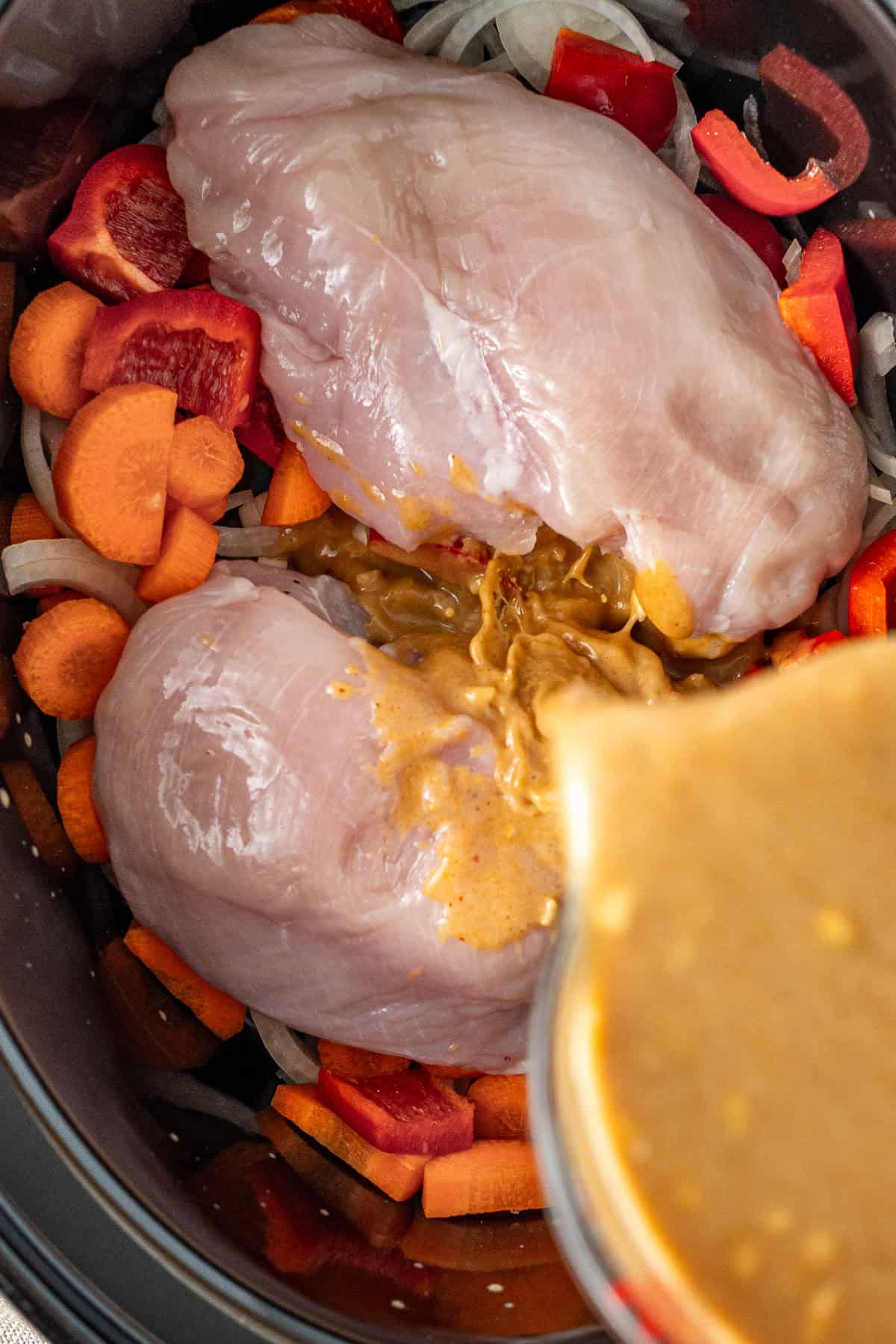 Pouring the satay sauce over the chicken in the slow cooker.