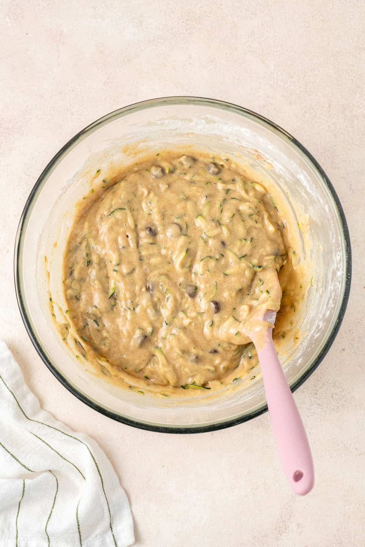 The zucchini batter in a glass bowl with a spatula.