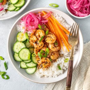 A colourful rice bowl with honey garlic prawns, pickled red onions, cucumber and carrot.
