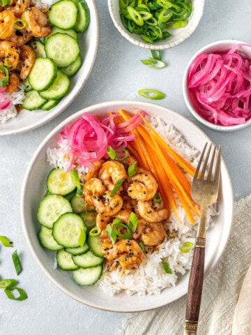 A colourful rice bowl with honey garlic prawns, pickled red onions, cucumber and carrot.