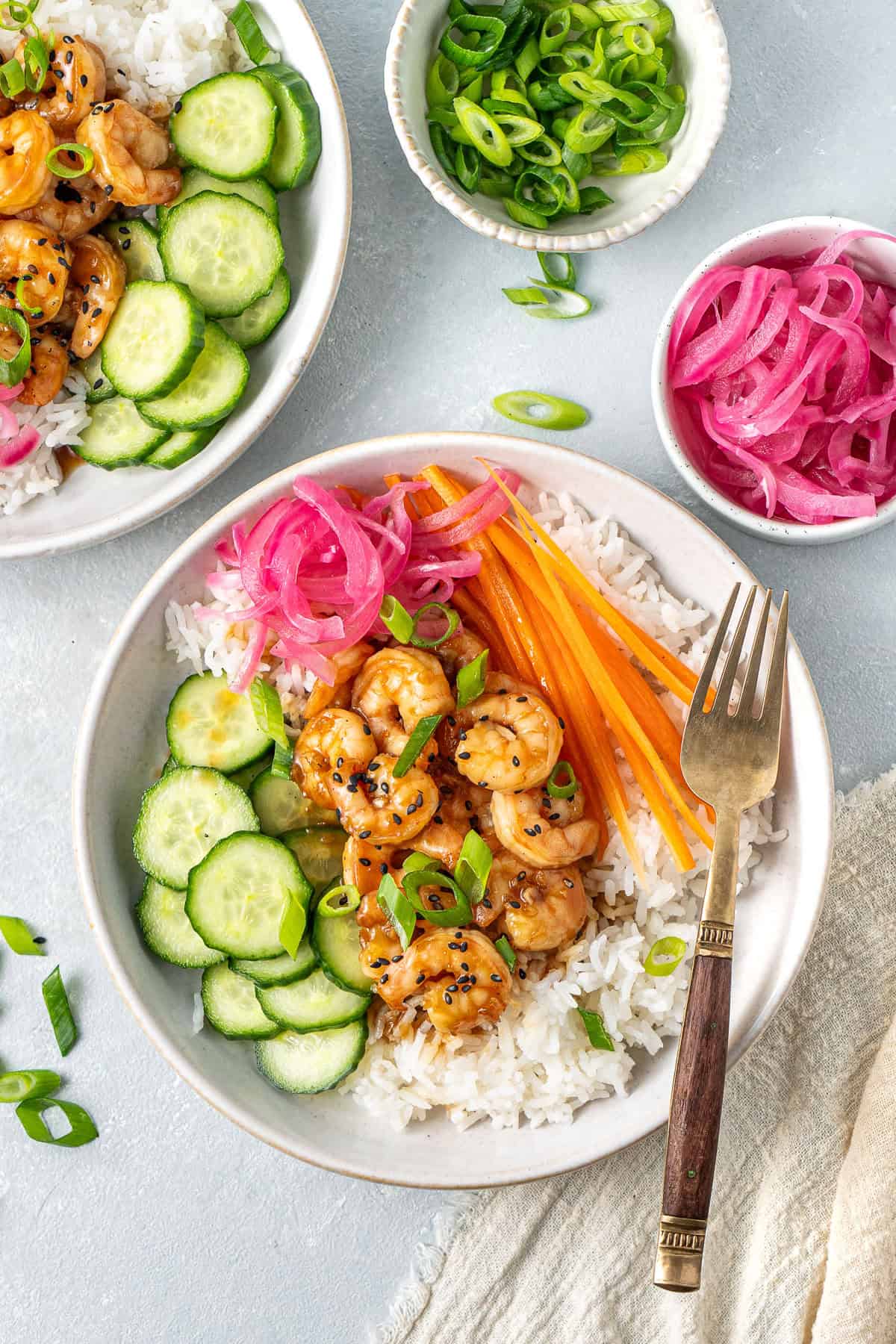 A colourful rice bowl with honey garlic prawns, pickled red onions, cucumber and carrot.