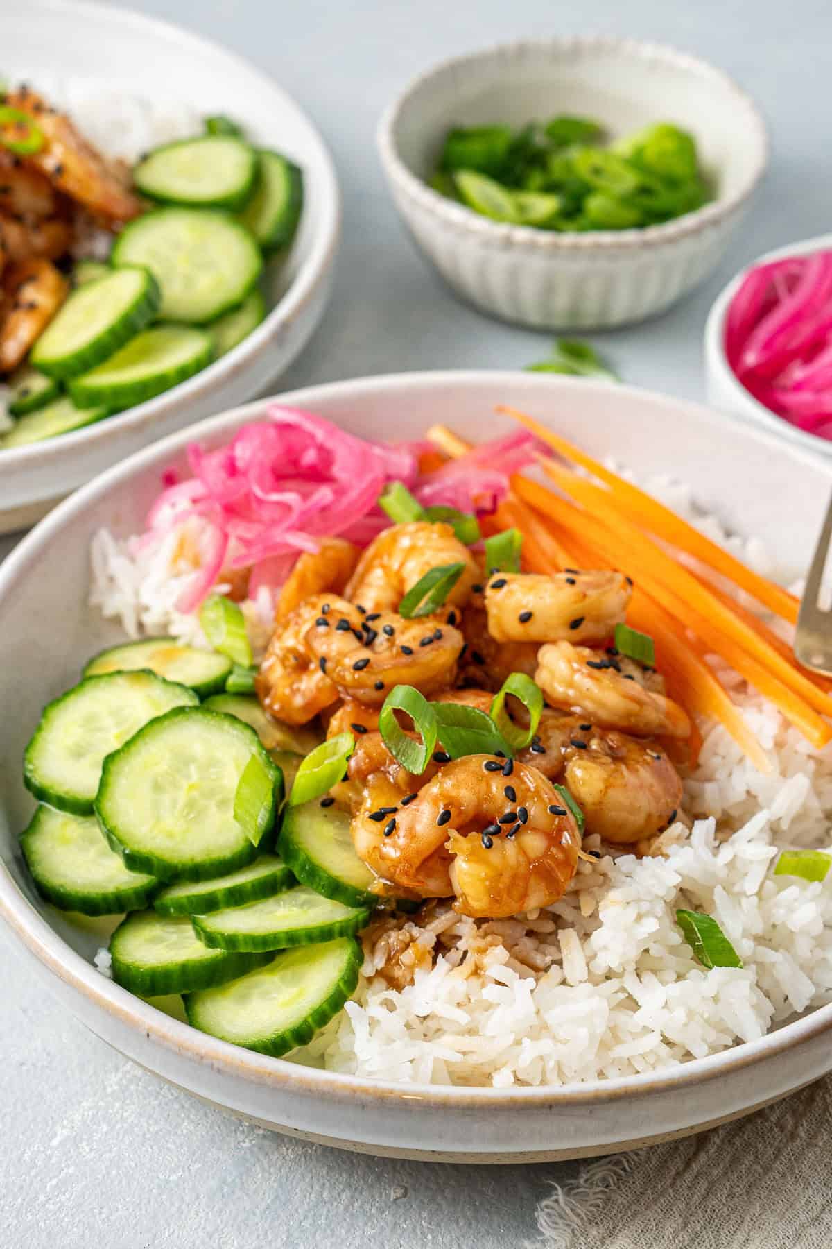 Close up of a honey garlic prawn rice bowl with pickled red onions, cucumber and carrot.