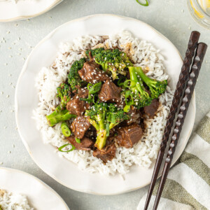 Beef and broccoli served onto plates with rice and chopsticks.
