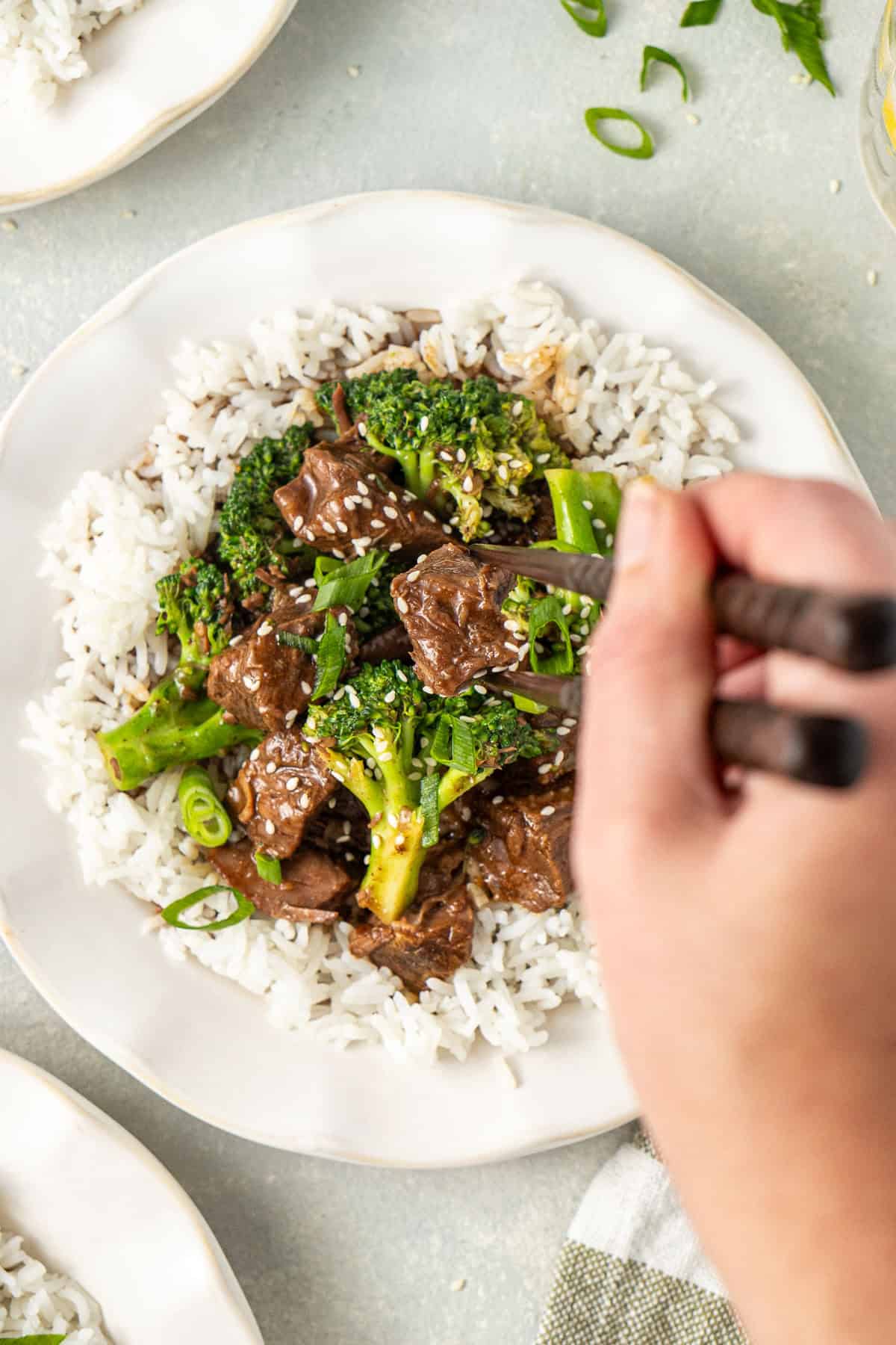 A hand taking a bite of slow cooker beef and broccoli and rice with chopsticks.