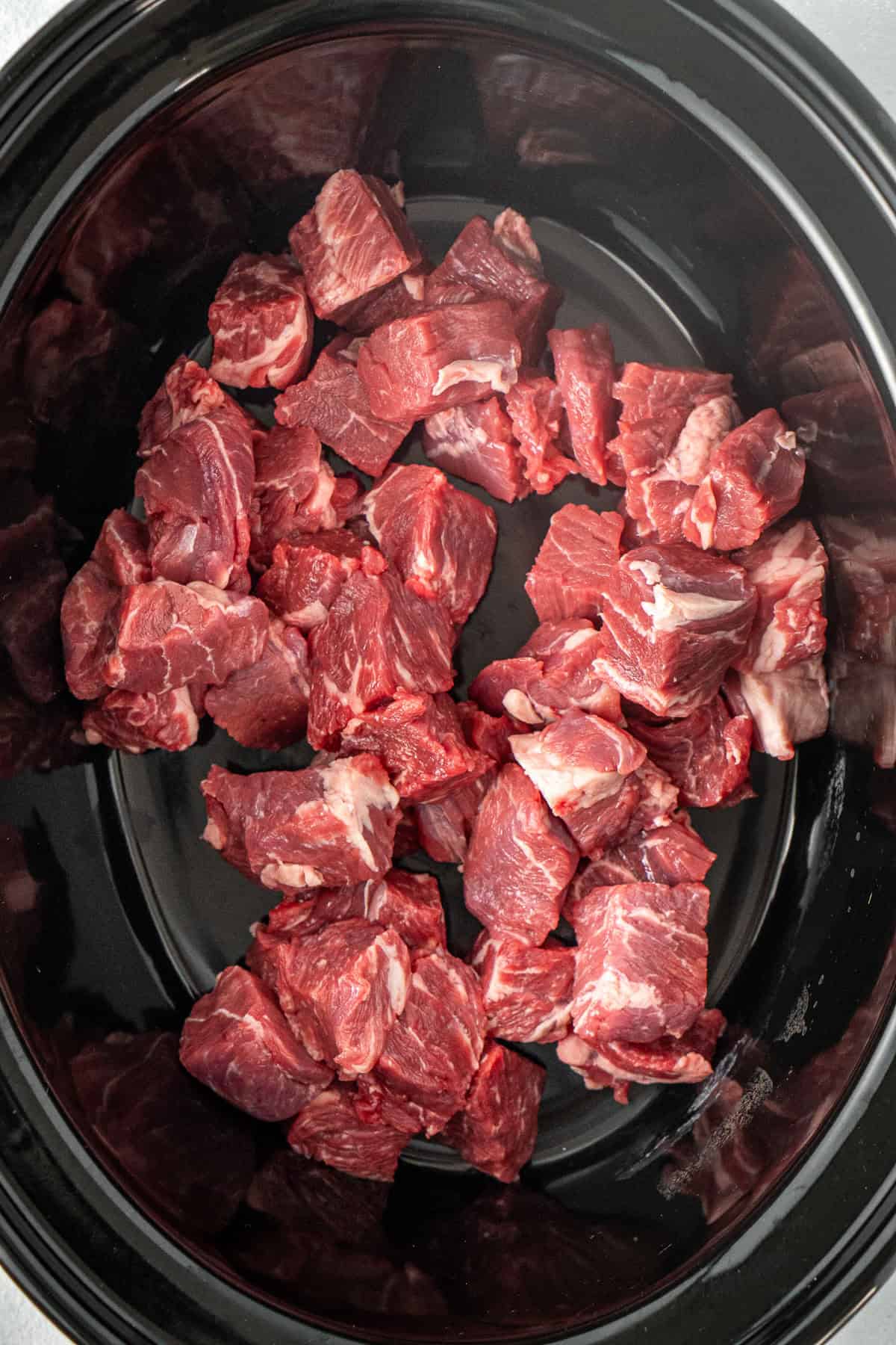 The chuck steak pieces in the bowl of the slow cooker.