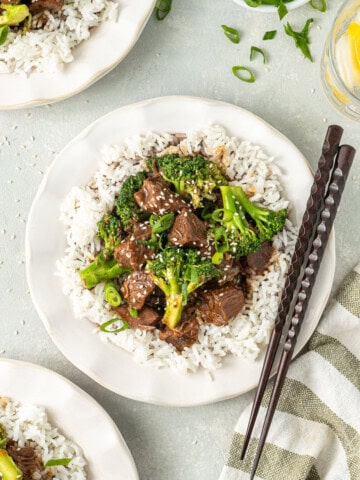 Beef and broccoli served onto plates with rice and chopsticks.