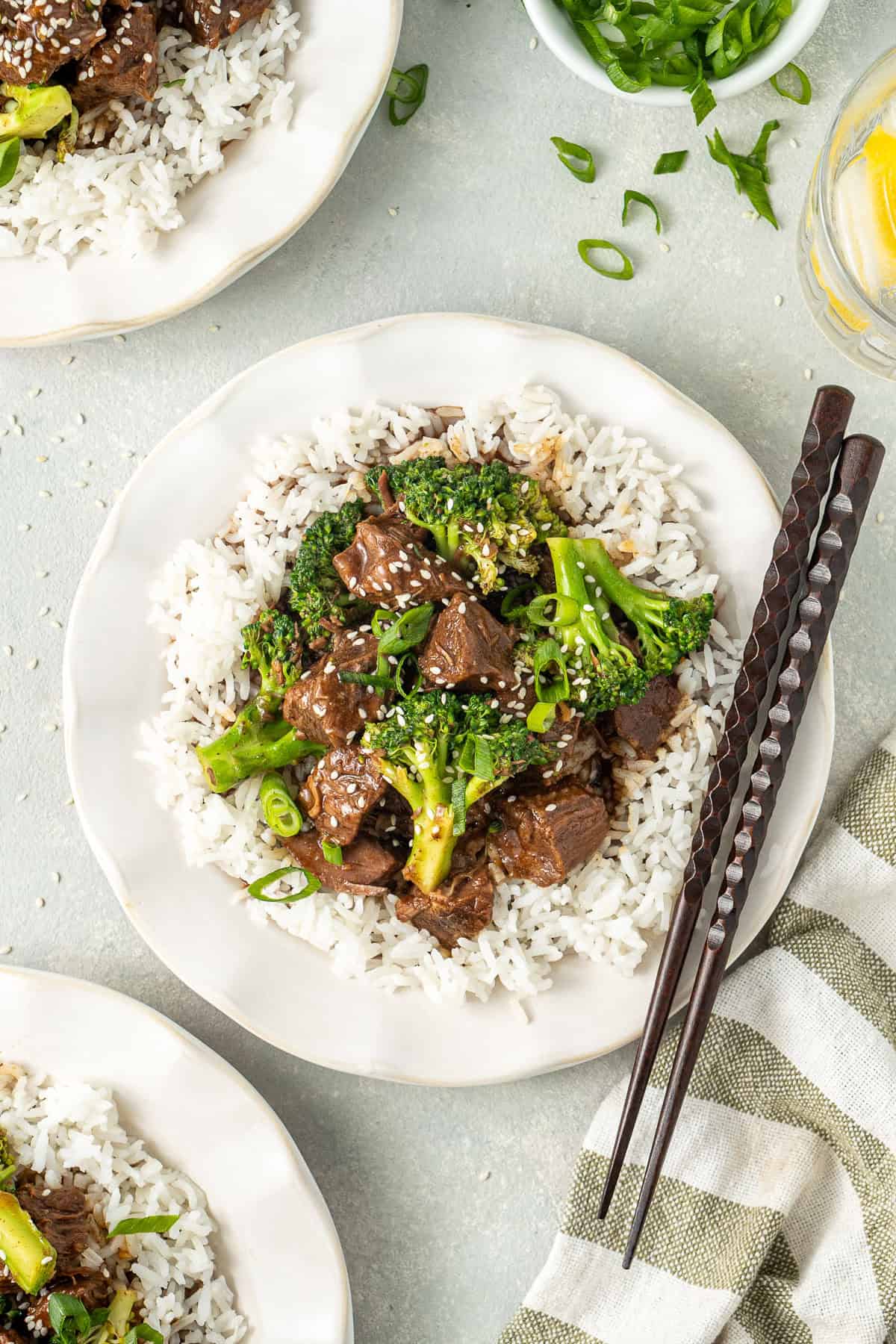 Beef and broccoli served onto plates with rice and chopsticks.