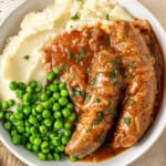 Slow cooker devilled sausages served in bowls on mashed potato with peas.
