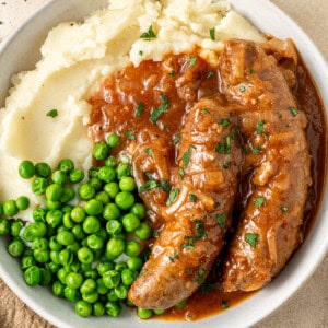Slow cooker devilled sausages served in bowls on mashed potato with peas.