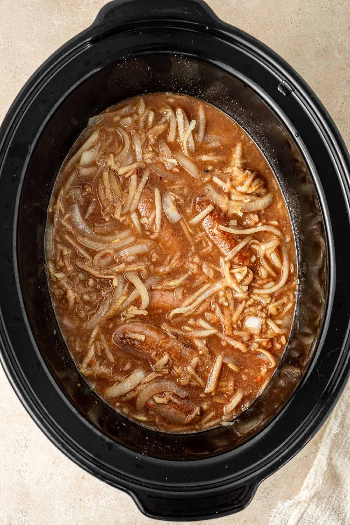 The sauce poured over the sausages and onions in the slow cooker.