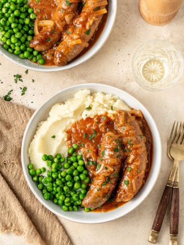 Slow cooker devilled sausages served in bowls on mashed potato with peas.